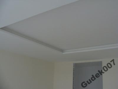 Pomieszczenie po malowaniu agregatem w Łodzi i okolicach: gładka, jasna ściana i sufit z dekoracyjną listwą przysufitową, widoczny narożnik pokoju i fragment okna.